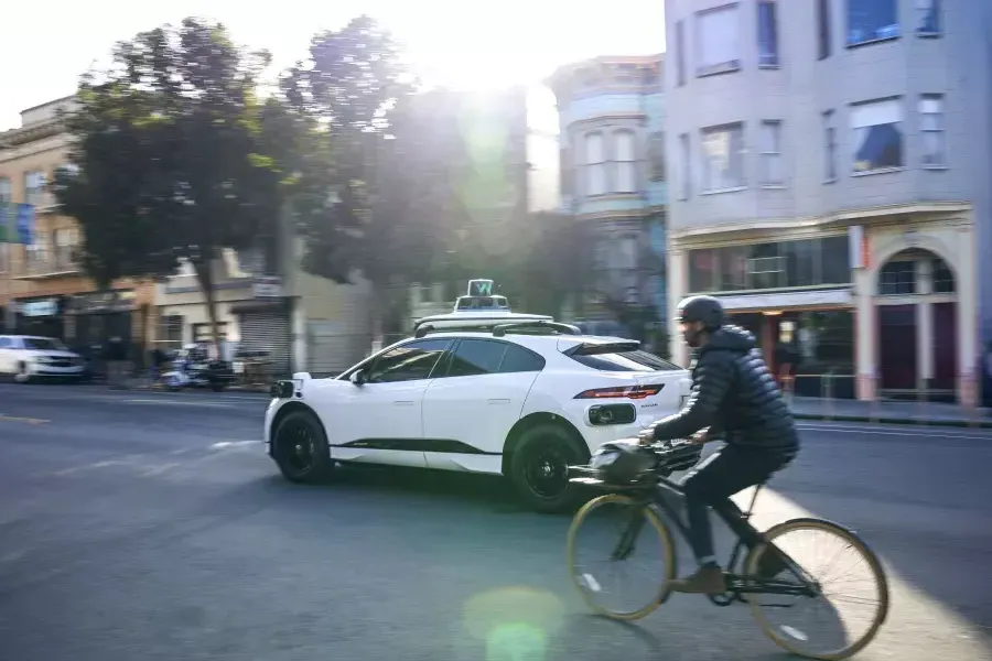 Person riding a bicycle behind a Waymo car